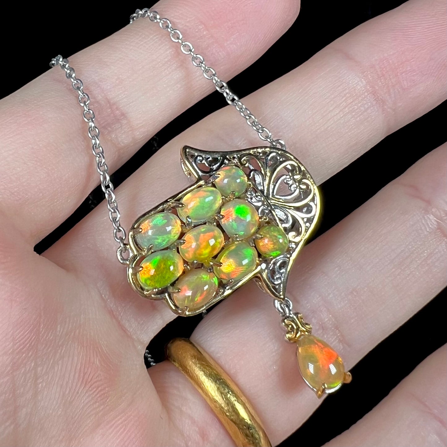 A Jewish opal hamsa necklace made from two-tone sterling silver, shown at an angle in a hand.