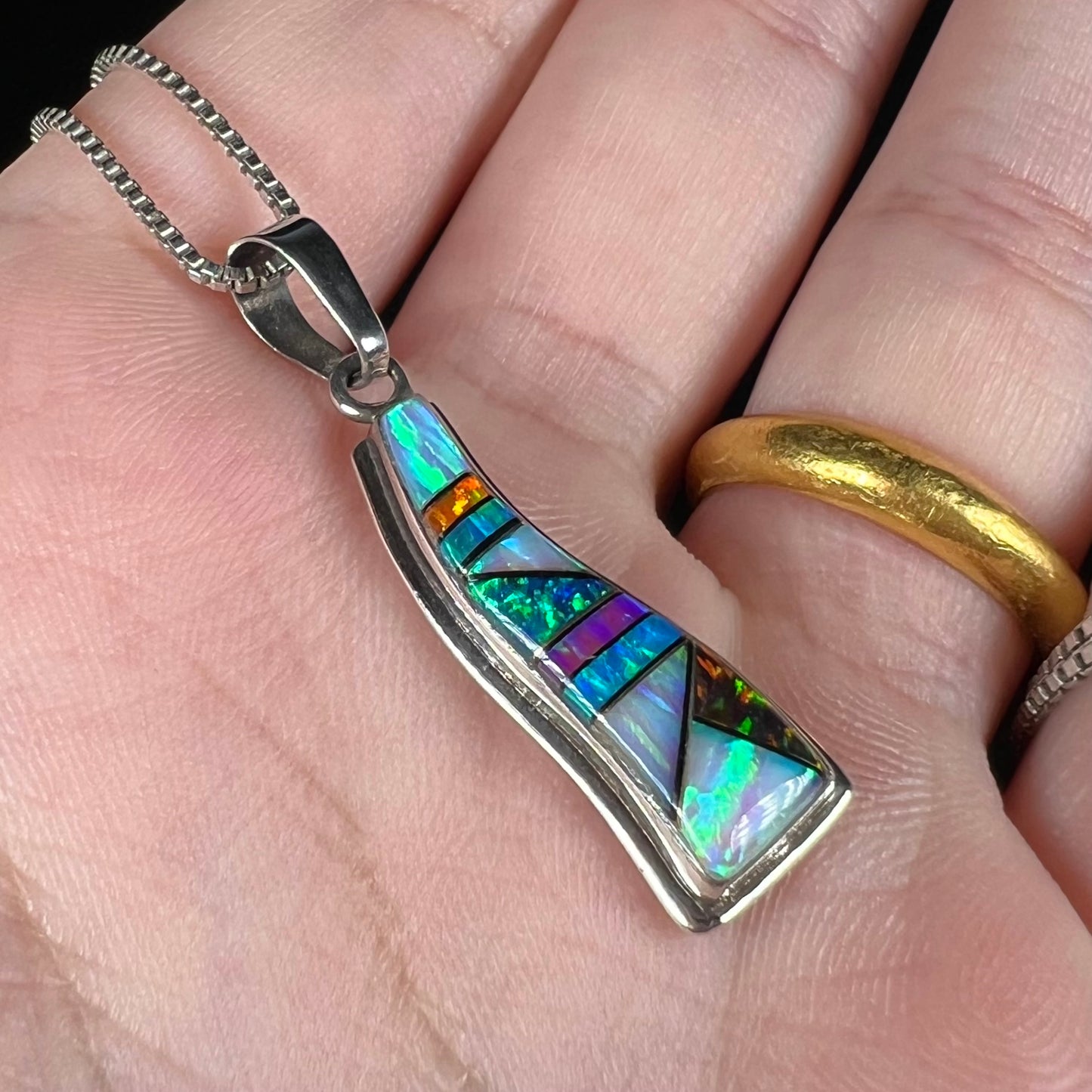 A lab-created opal inlay pendant in sterling silver, made by artist Johnson Ralph, shown at an angle in a hand.