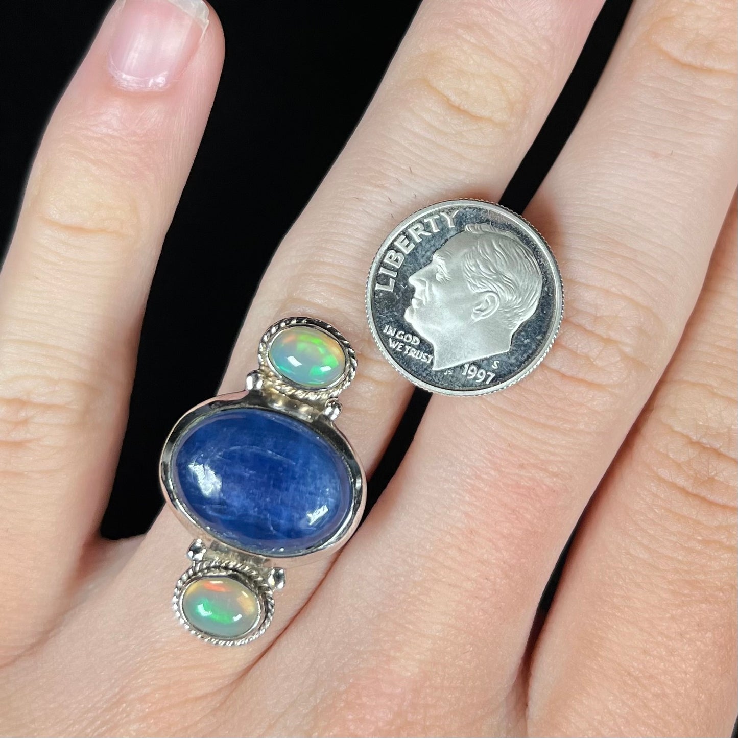 A sterling silver kyanite and opal cabochon ring worn on a finger next to a dime coin.