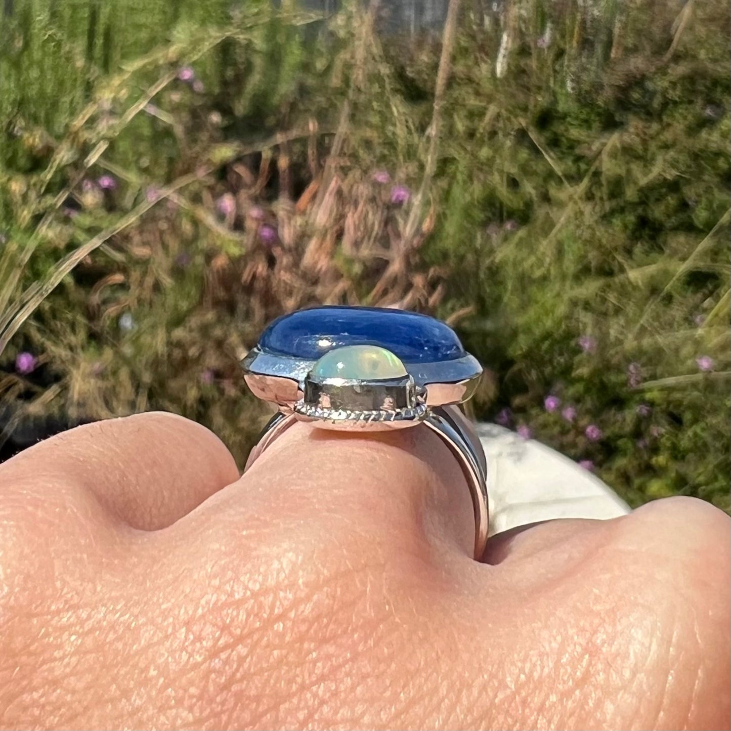 Side gallery view of a kyanite opal ring worn on a finger in natural daylight The stones are not very visible.