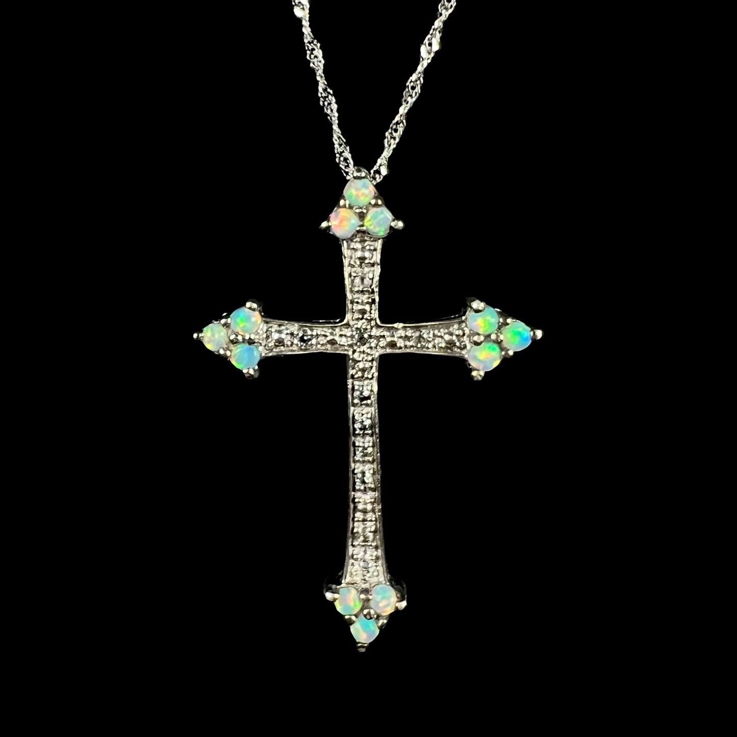 A silver lab-created opal cross necklace with CZ accents shown from the front against a black background.