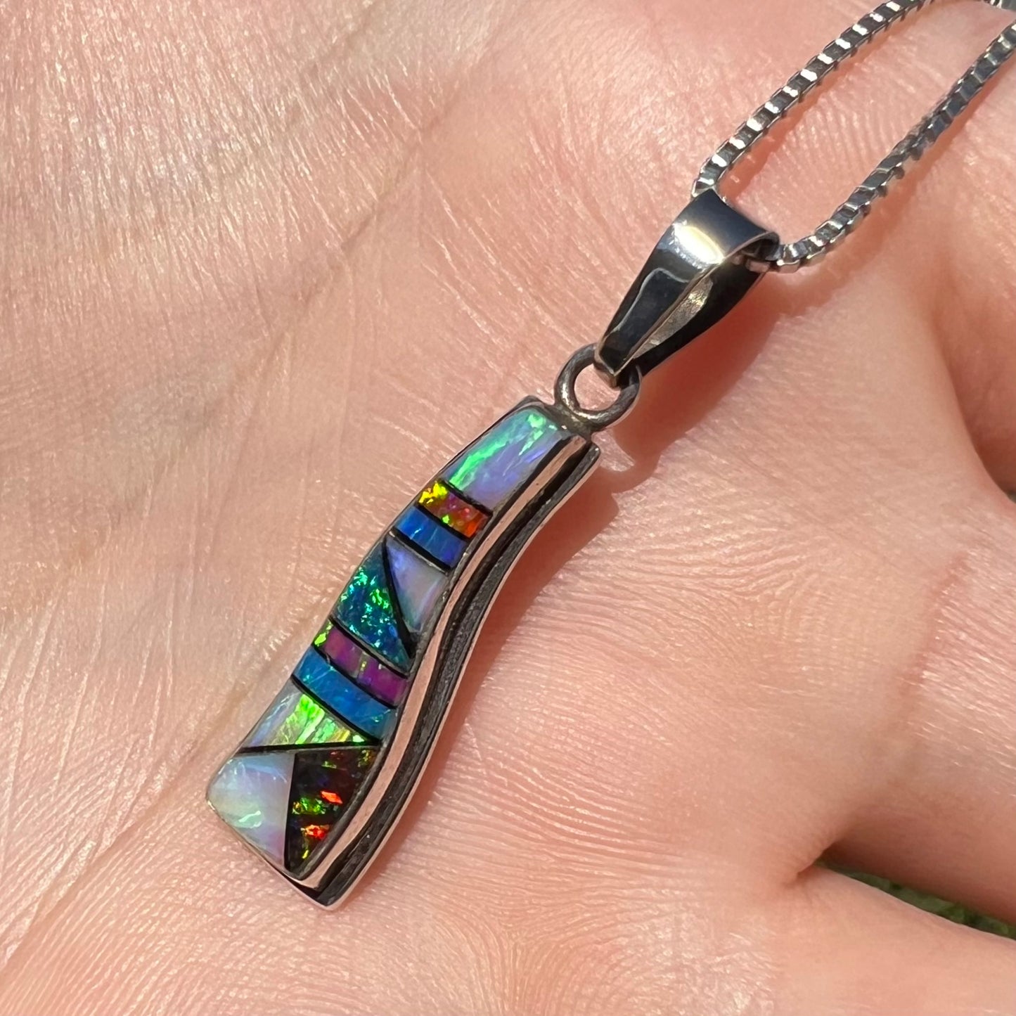 A lab-created opal inlay necklace shown and held at a close-up angle in the sunlight.