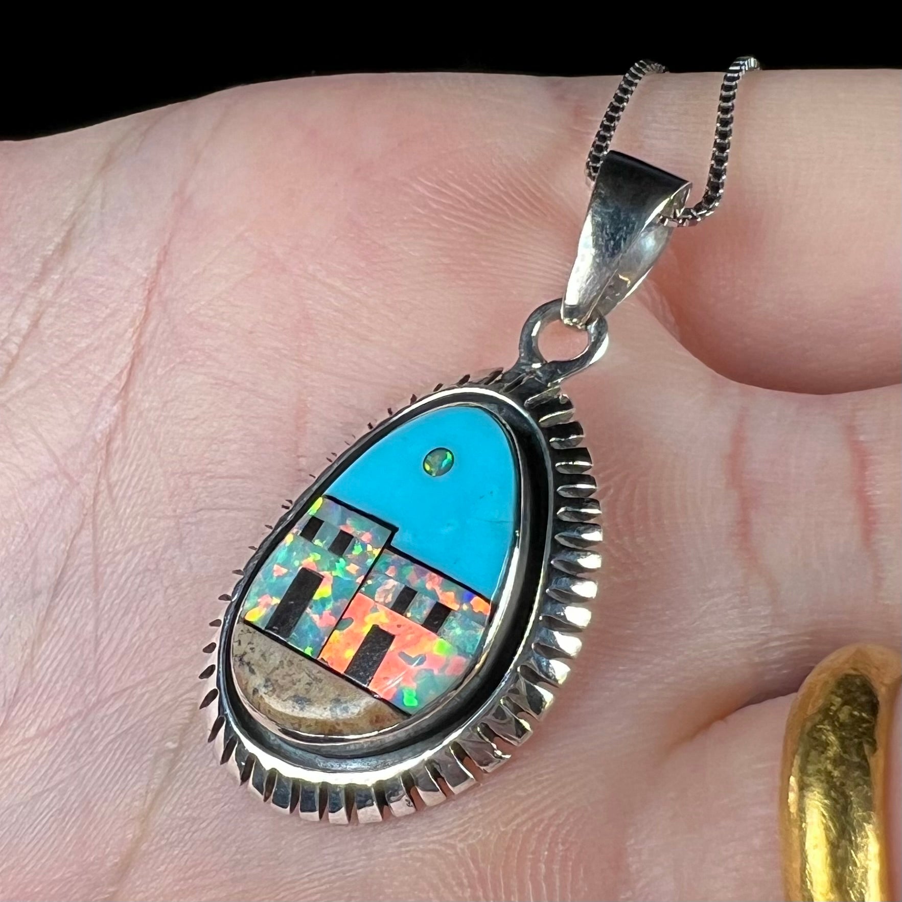 Angled view of a Southwest-style silver lab-created opal and turquoise inlay necklace, shown close-up in a hand.