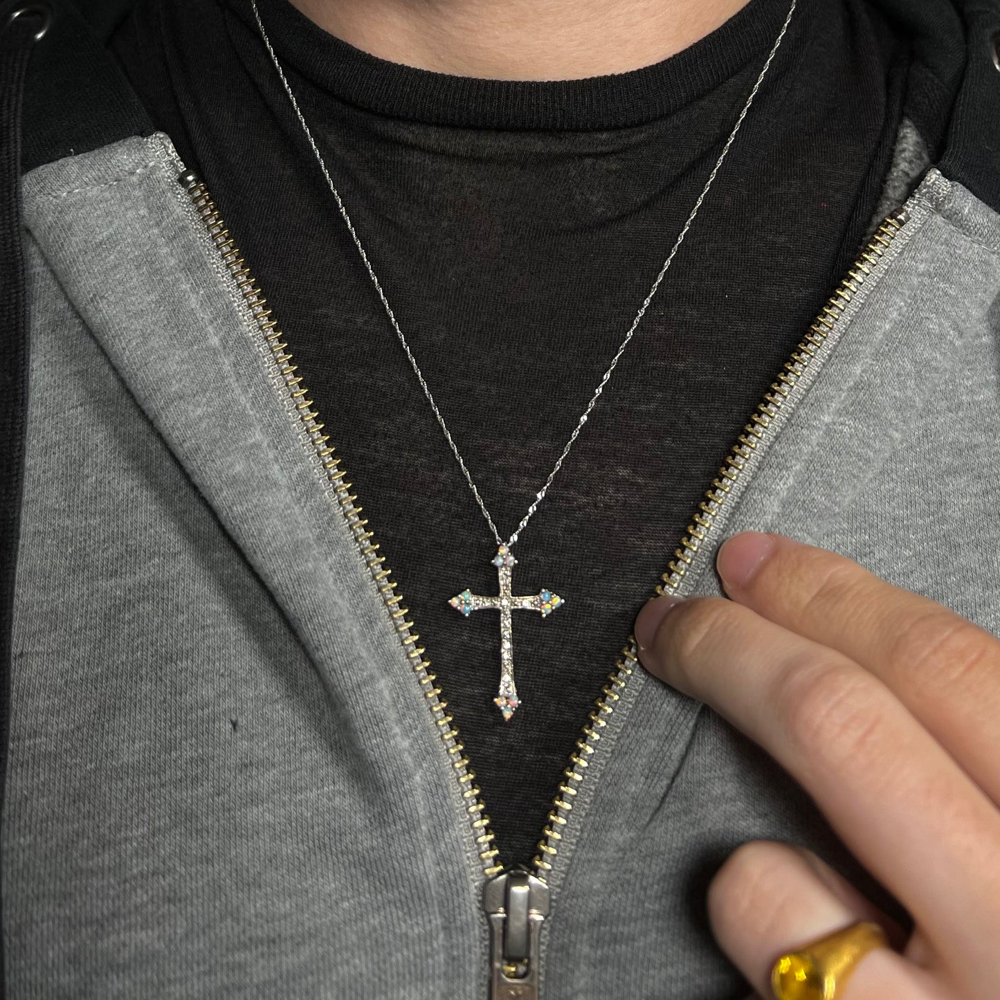 A lab-created opal cross necklace worn on a dark shirt under a partially unzipped hoodie.