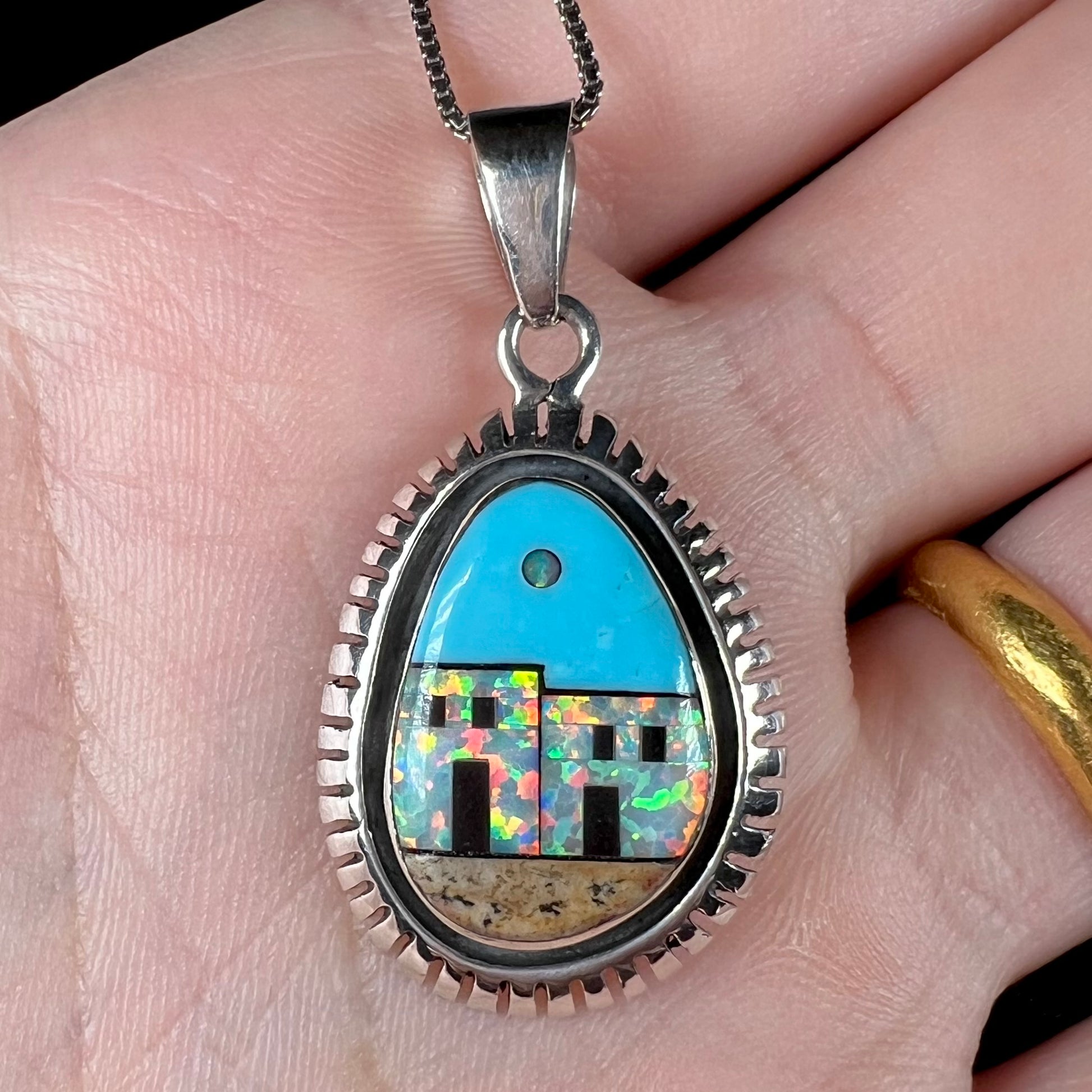 A Southwest-style silver lab-created opal and turquoise inlay necklace, shown close-up in a hand.