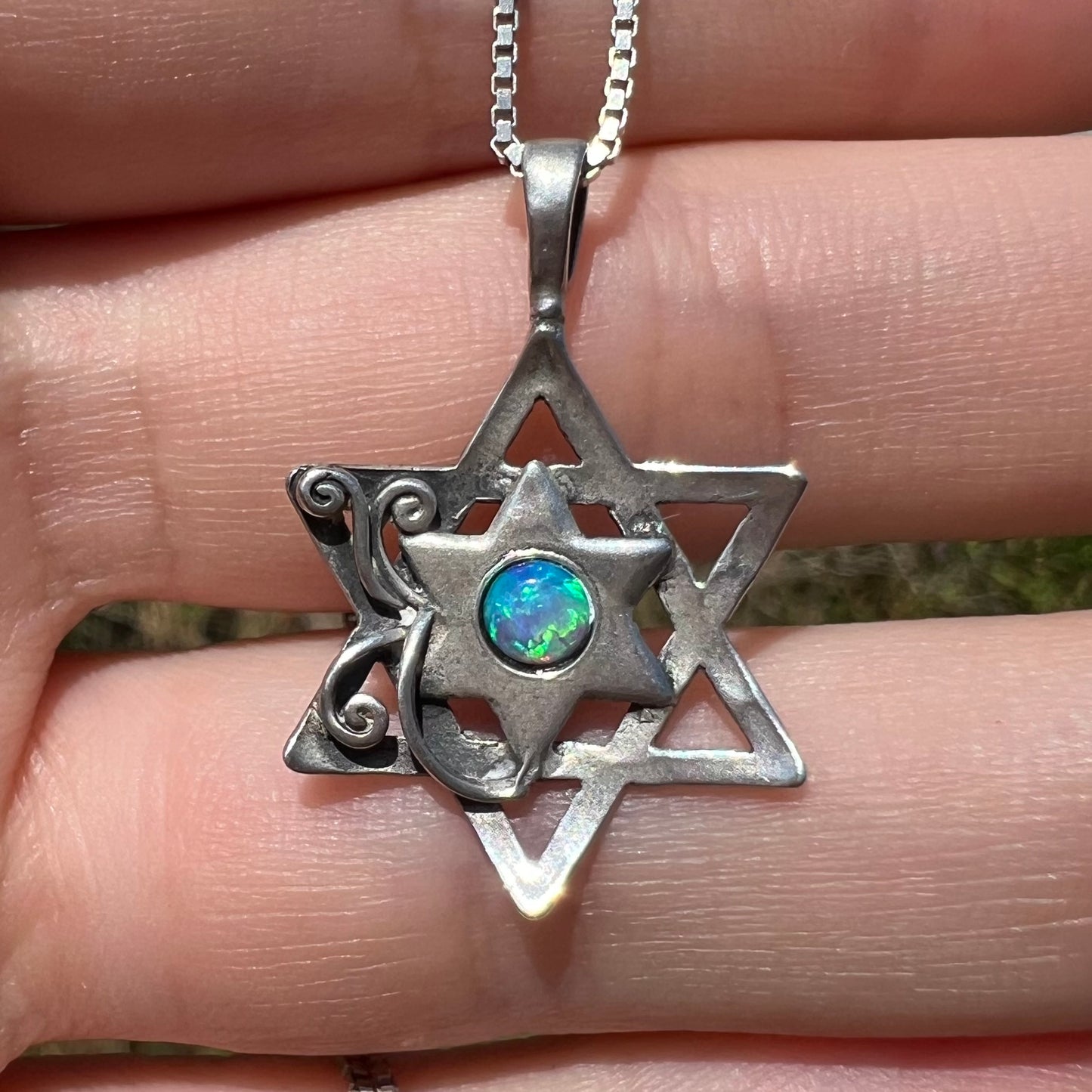 Front close-up of a silver Star of David necklace set with a round blue lab-created opal in sunlight.