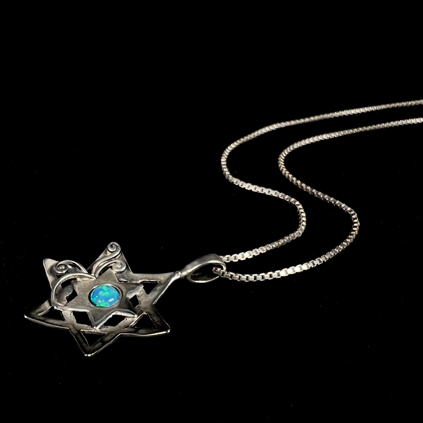 A lab-created opal Star of David necklace laying against a black background.