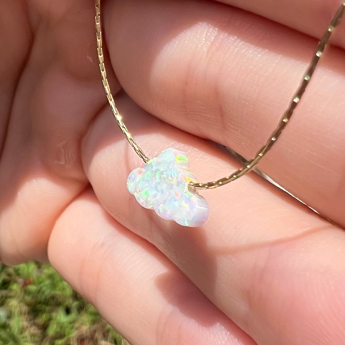A lab opal cloud necklace held at a sharp angle in daylight.