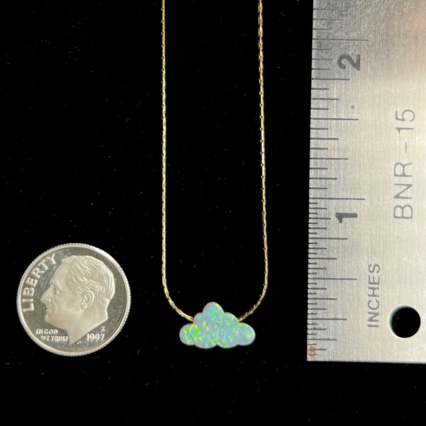 A lab-created opal cloud necklace on a gold filled chain next to a dime coin and ruler for scale.