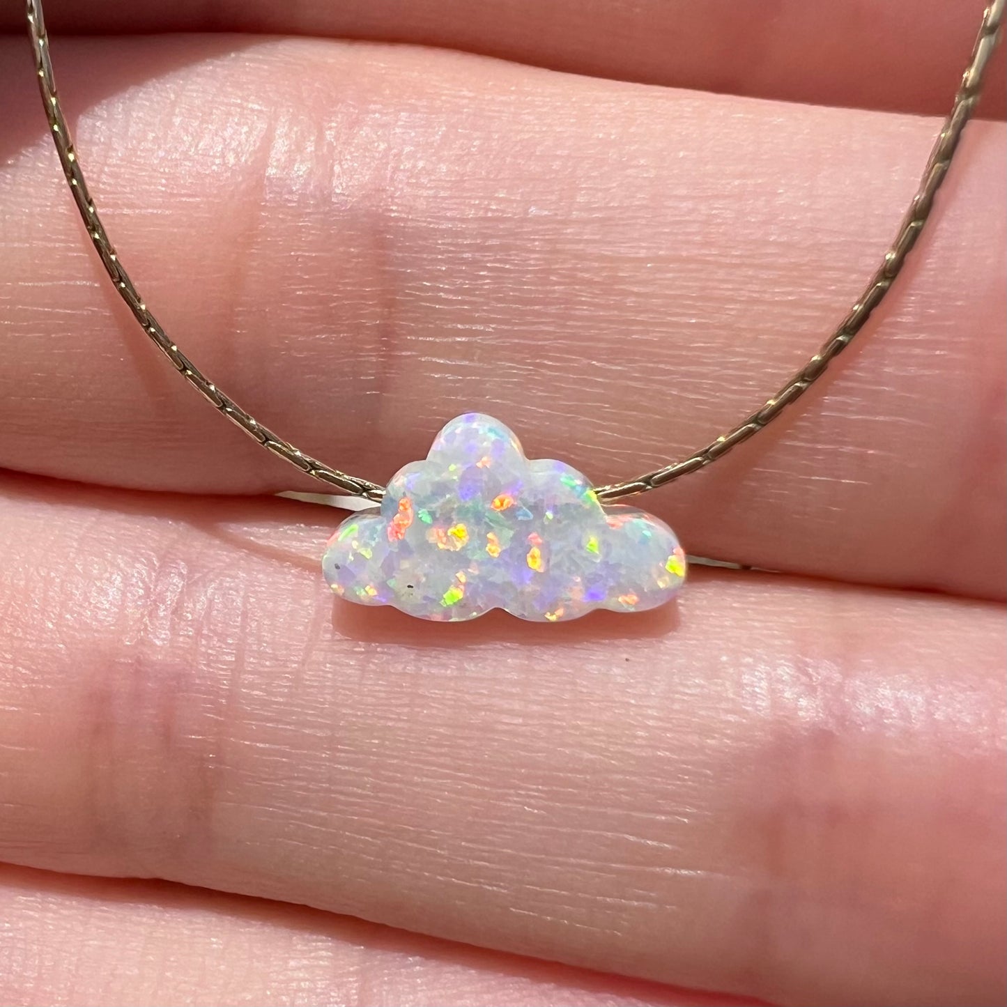 Close-up front view of a lab-created opal cloud necklace held by a hand in the sunlight.