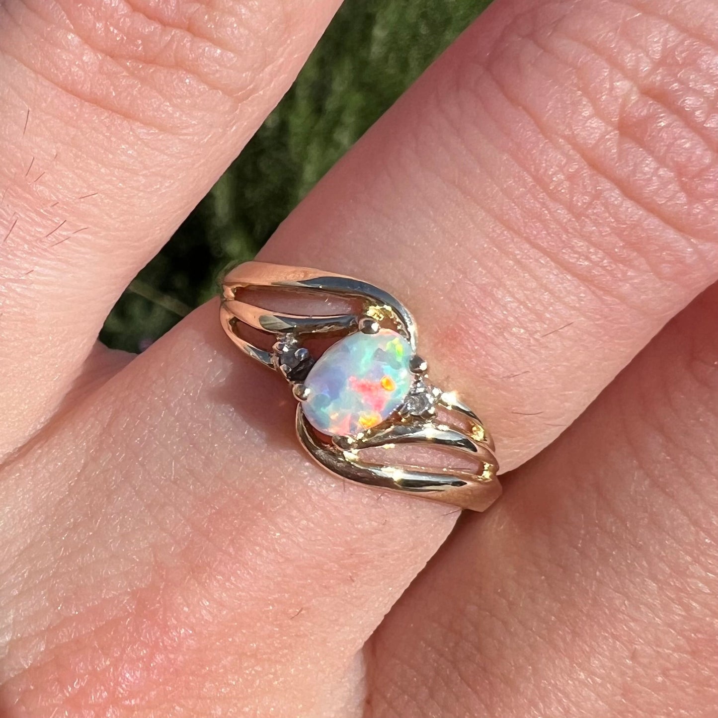 A yellow gold ring mounted with two diamond accents and an oval cut lab created opal. The opal has bright red colors.