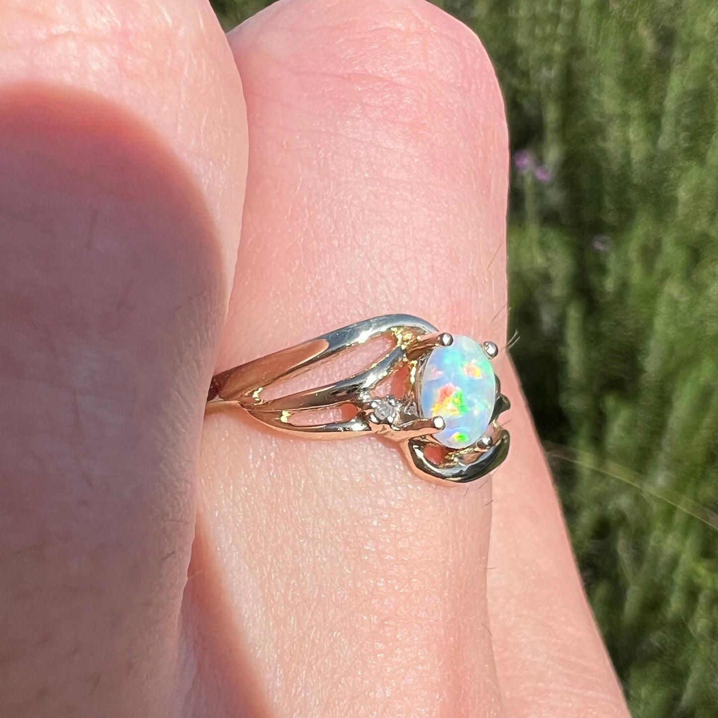 A yellow gold ring mounted with two diamond accents and an oval cut lab created opal. The opal has bright red colors.