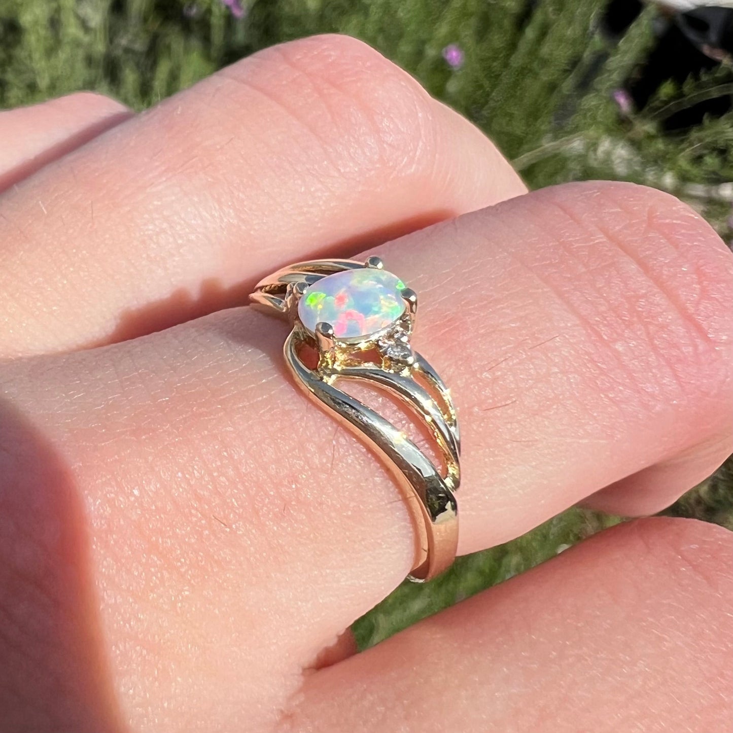 A yellow gold ring mounted with two diamond accents and an oval cut lab created opal. The opal has bright red colors.