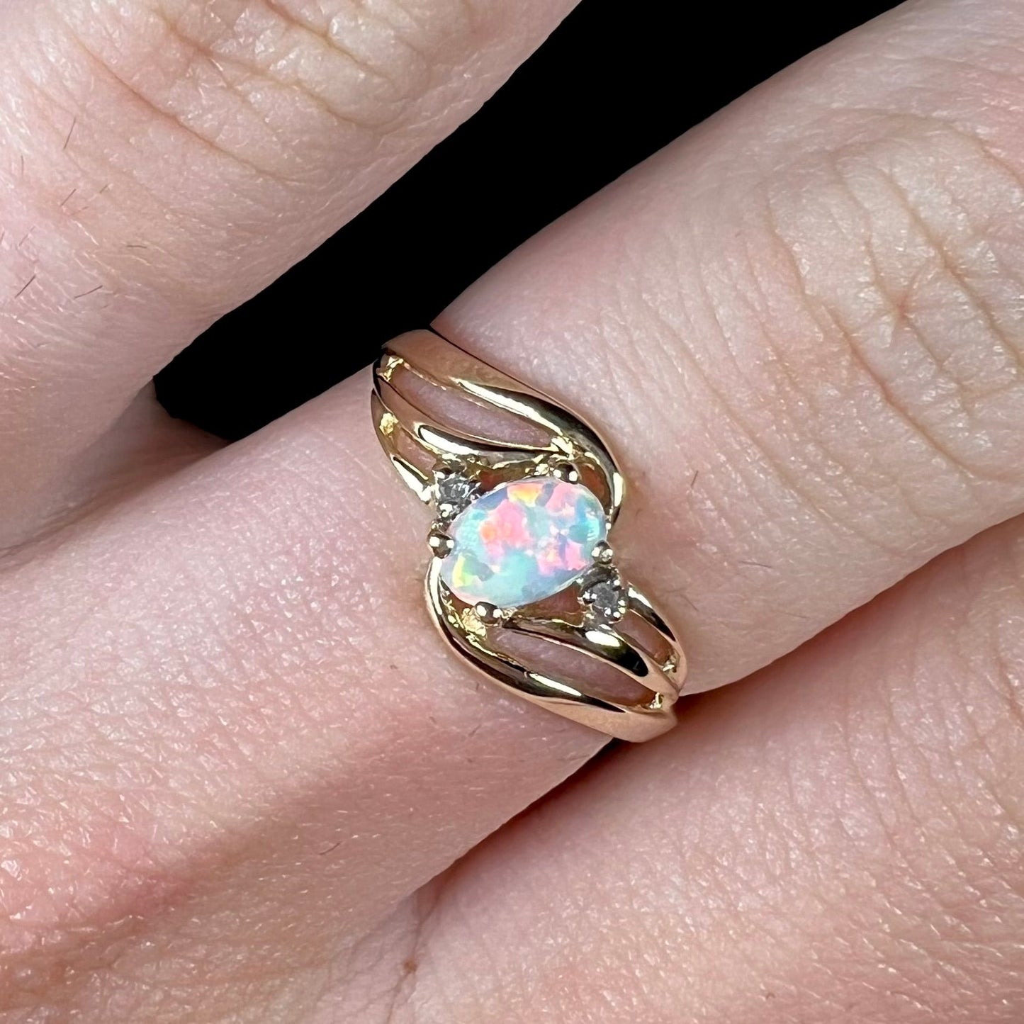 A yellow gold ring mounted with two diamond accents and an oval cut lab created opal. The opal has bright red colors.