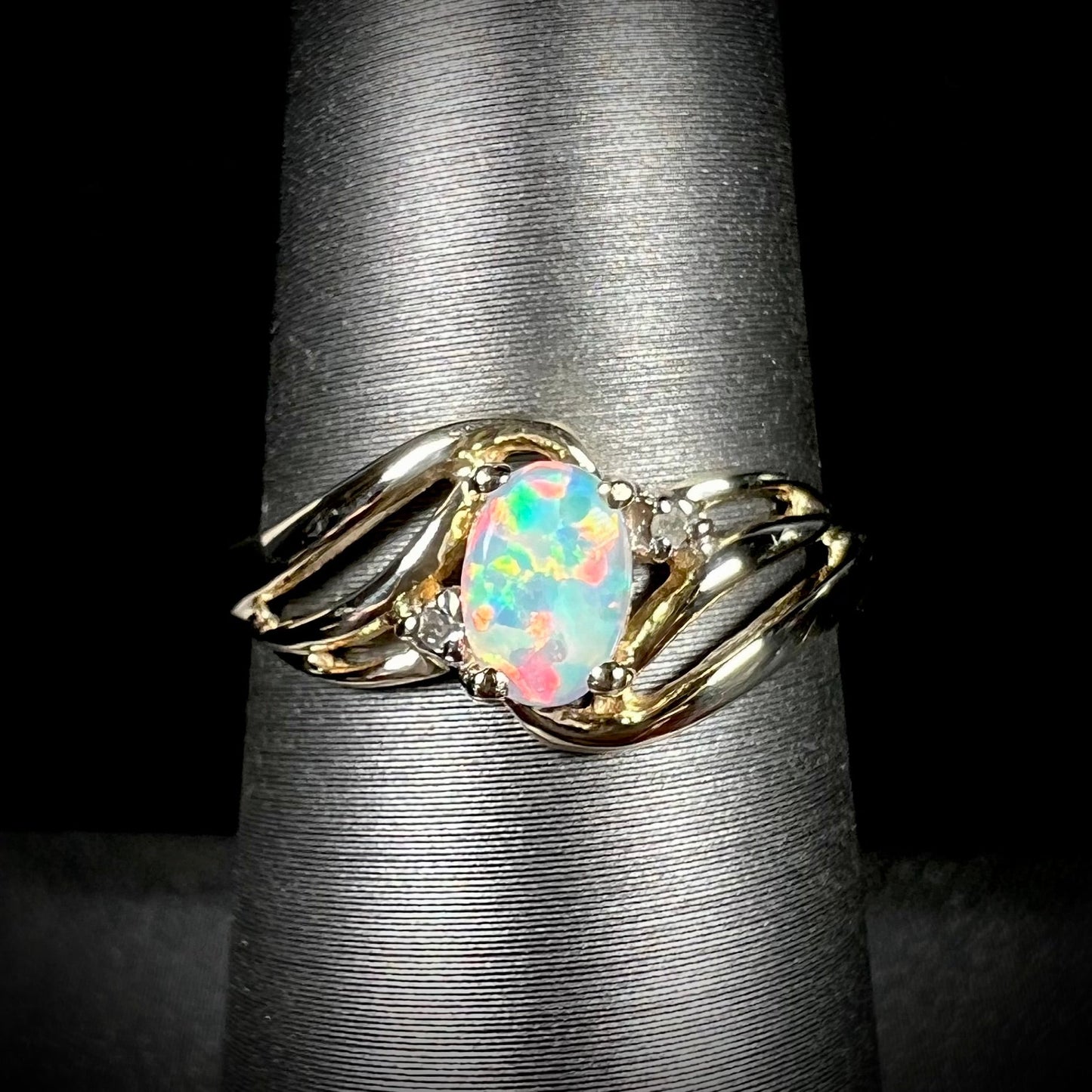 A yellow gold ring mounted with two diamond accents and an oval cut lab created opal. The opal has bright red colors.