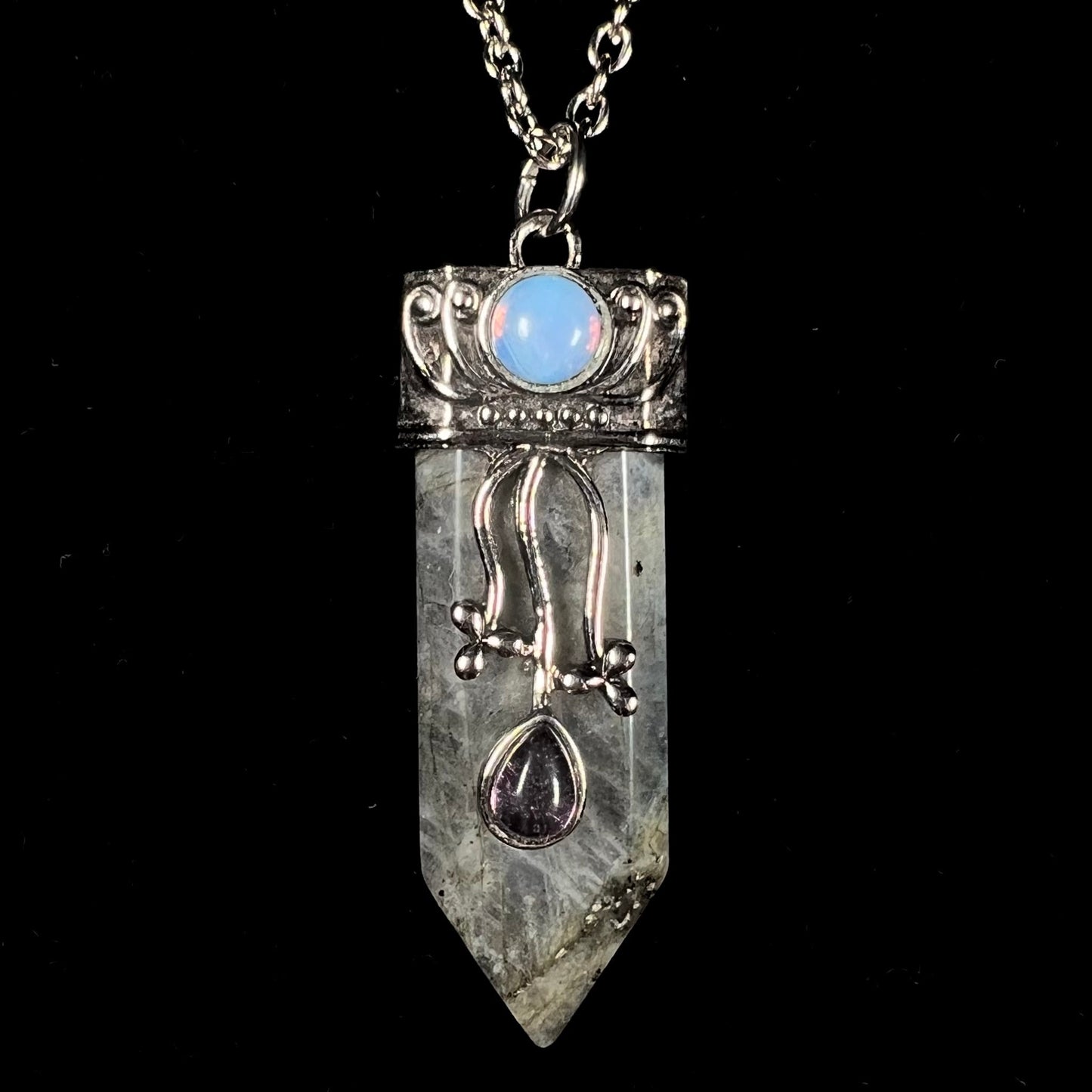 A stainless steal necklace set with a crystal shaped labradorite stone, purple glass, and an opalite accent.