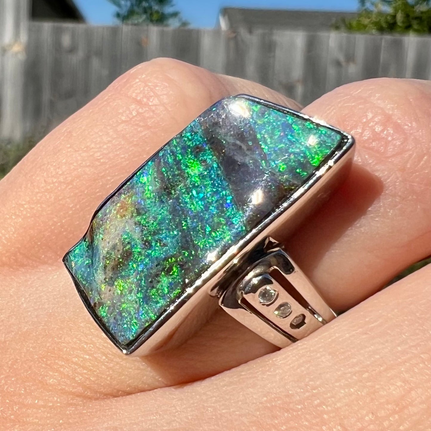 A ladies' green Australian boulder opal and diamond ring in platinum, shown at an angle close-up in sunlight.