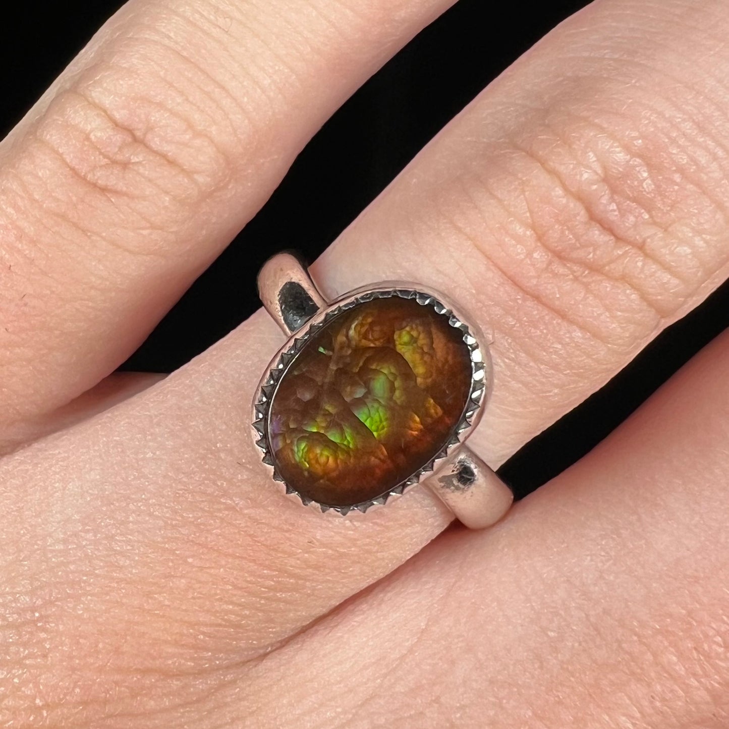 Close-up of finger wearing a ladies' fire agate ring against black background. The fire agate has green iridescence.
