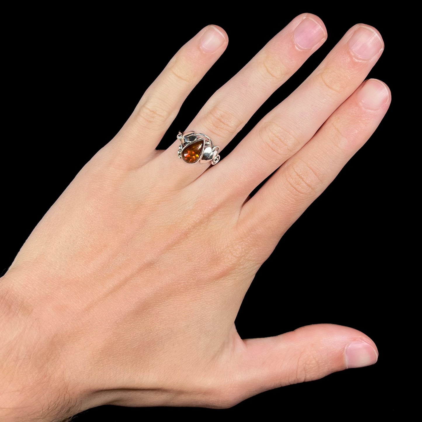 A ladies' pear shaped red fire agate ring with a sterling silver leaf design worn on a hand against a black background.
