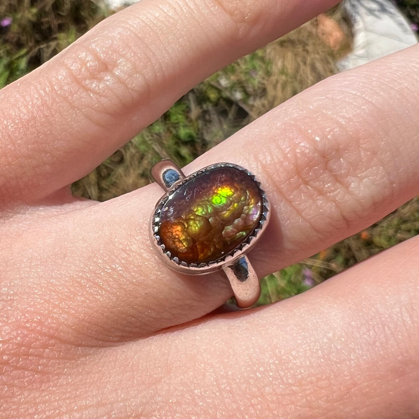 Close-up front view of a ladies' Mexican fire agate ring worn on a finger in natural sunlight.
