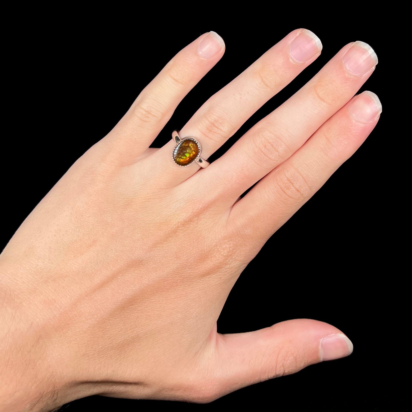 A hand wearing a ladies' sterling silver fire agate ring against a black background.