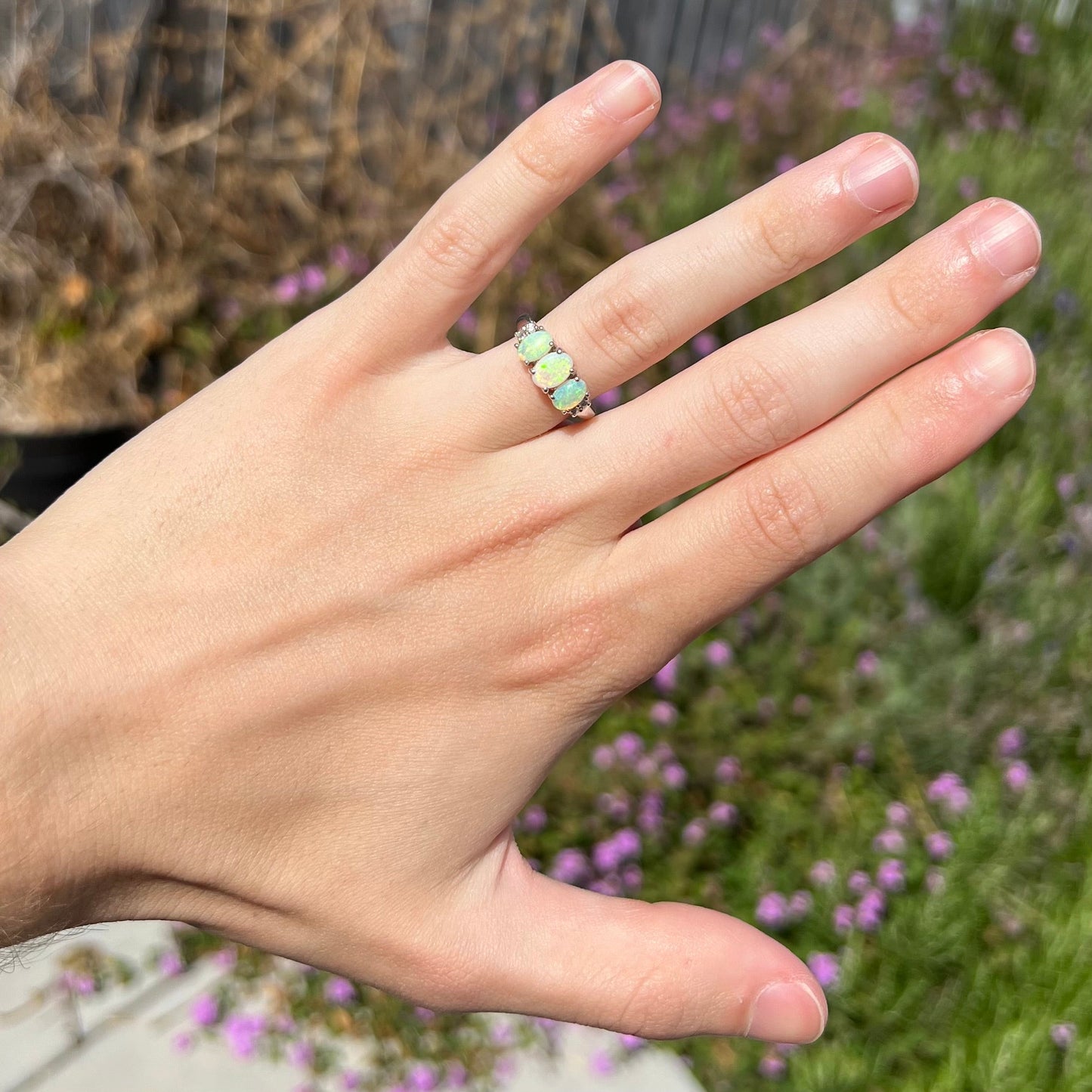 A ladies' white gold ring prong-set with three natural white opals and diamond accents. The opals play a green color.