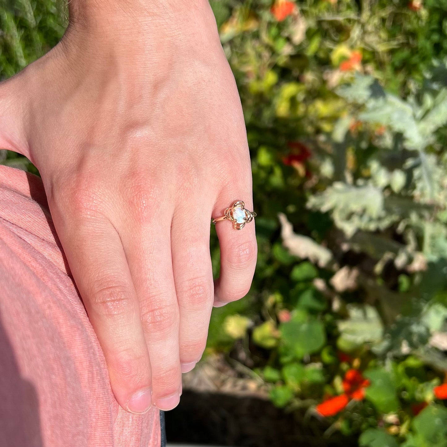 A yellow gold ring mounted with an oval cut opal. The opal has a white base tone with green and blue color play.