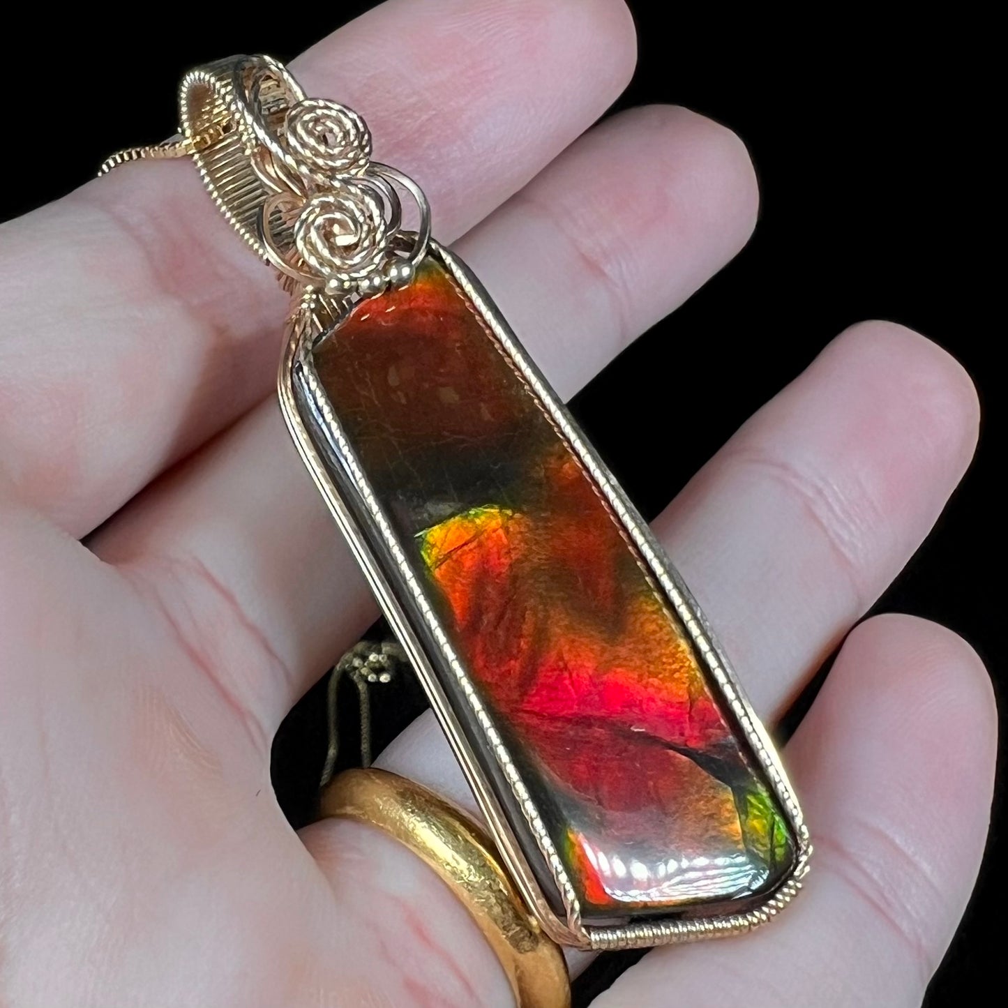 A large red ammolite pendant held at an angle in a hand against a black background.