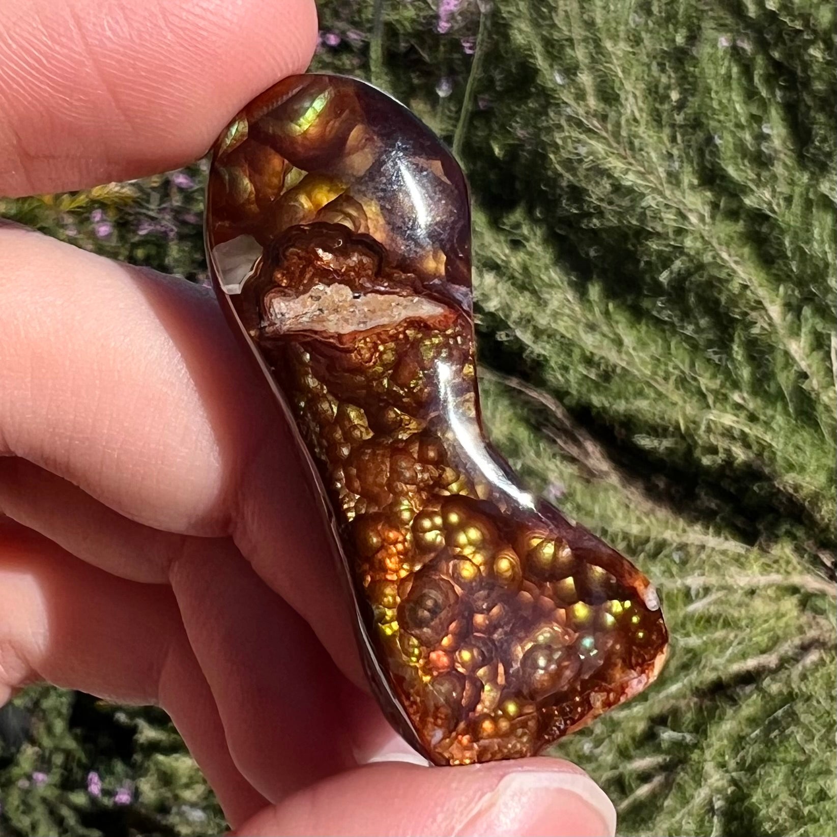A loose, freeform cabochon cut fire agate gemstone.  The stone exhibits a bubbly pattern.