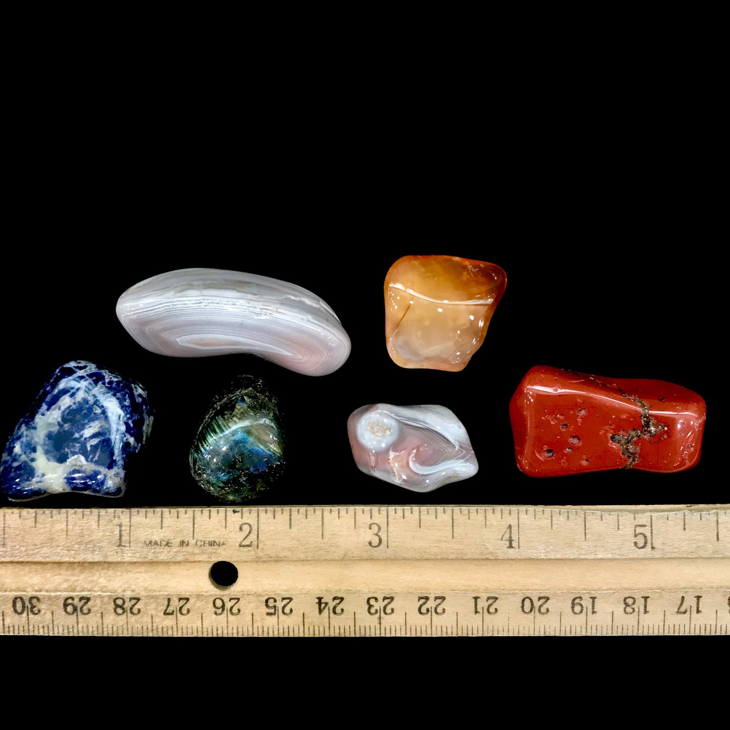 Six polished rocks being measured. Average length 1 inch to 2 inches.