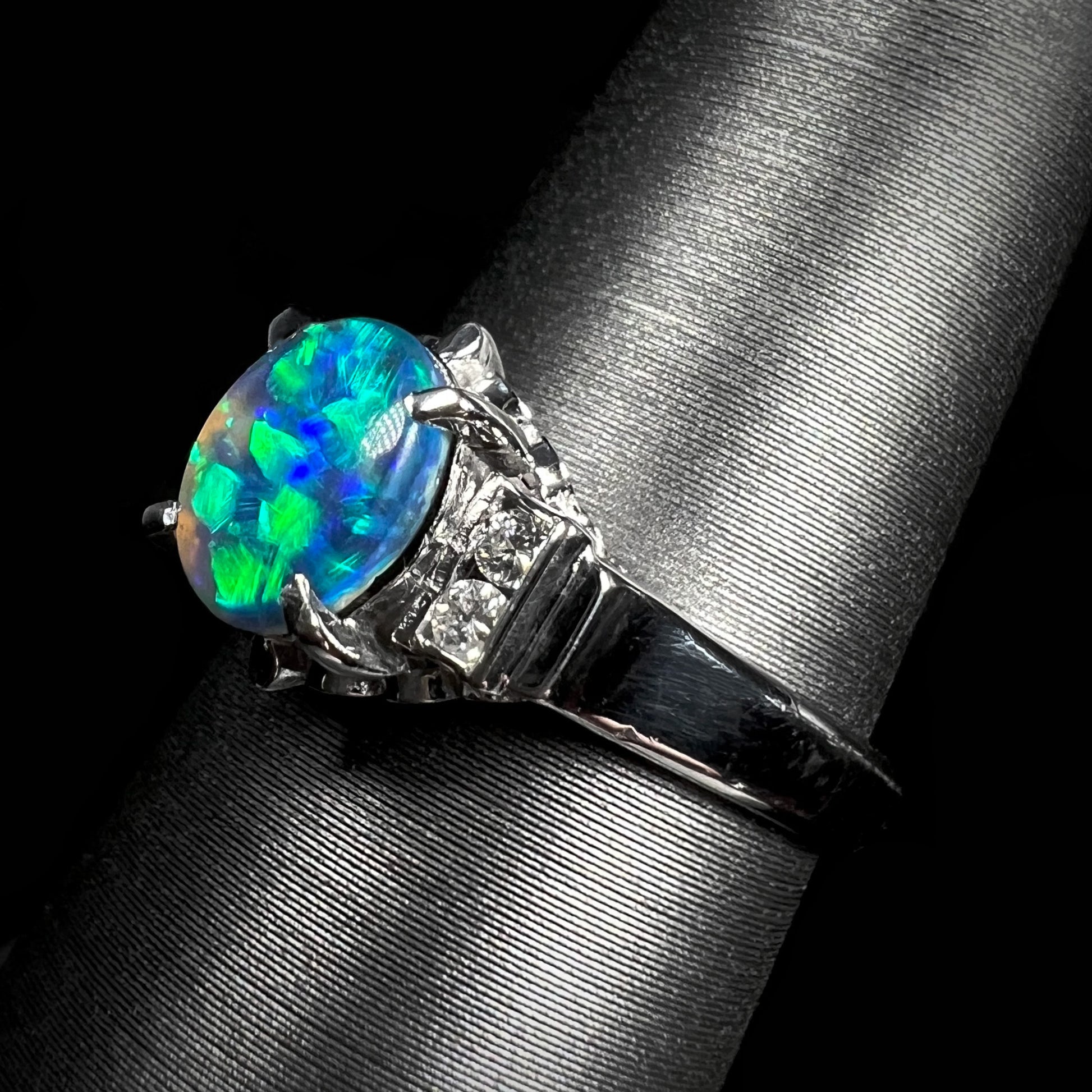 A Lightning Ridge black opal engagement ring in platinum, displaying a vibrant green fire with diamond accents and intricate filigree details.