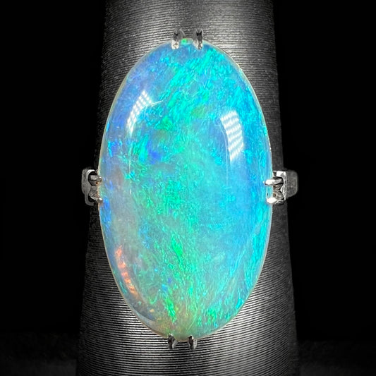 An Art Deco-inspired Lightning Ridge crystal opal ring in platinum. The opal displays vivid green and blue hues under LED lighting.