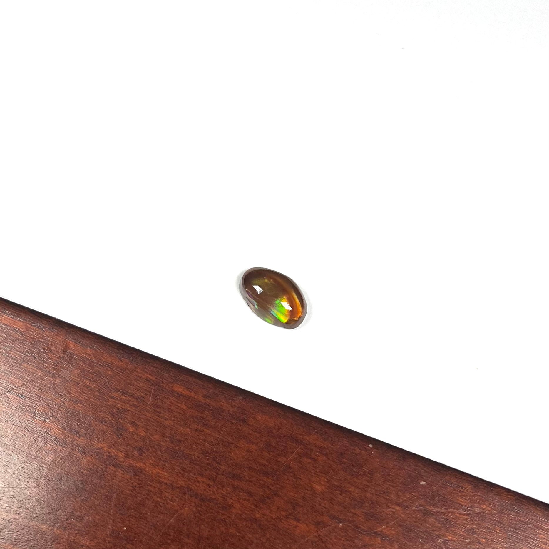 A loose, oval cabochon cut fire agate stone that shines red, yellow, green, blue, and purple.