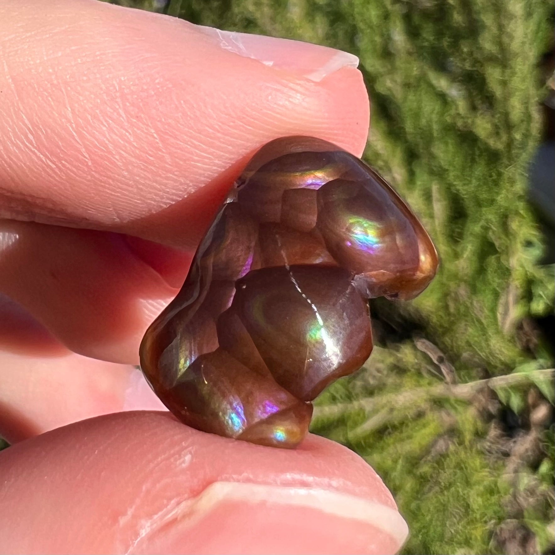 A polished, freeform shaped fire agate stone.  The stone is purple, green, and blue with red and yellow banding.