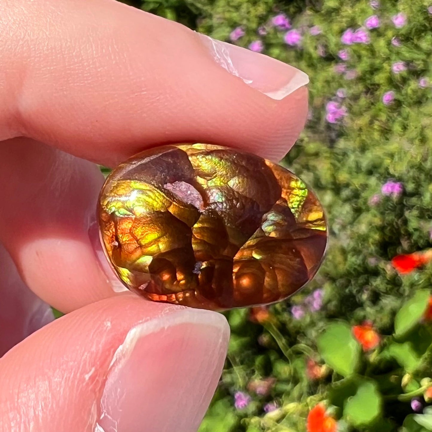 A loose, oval cabochon cut fire agate gemstone. The stone is bubbly green with blue overtones.