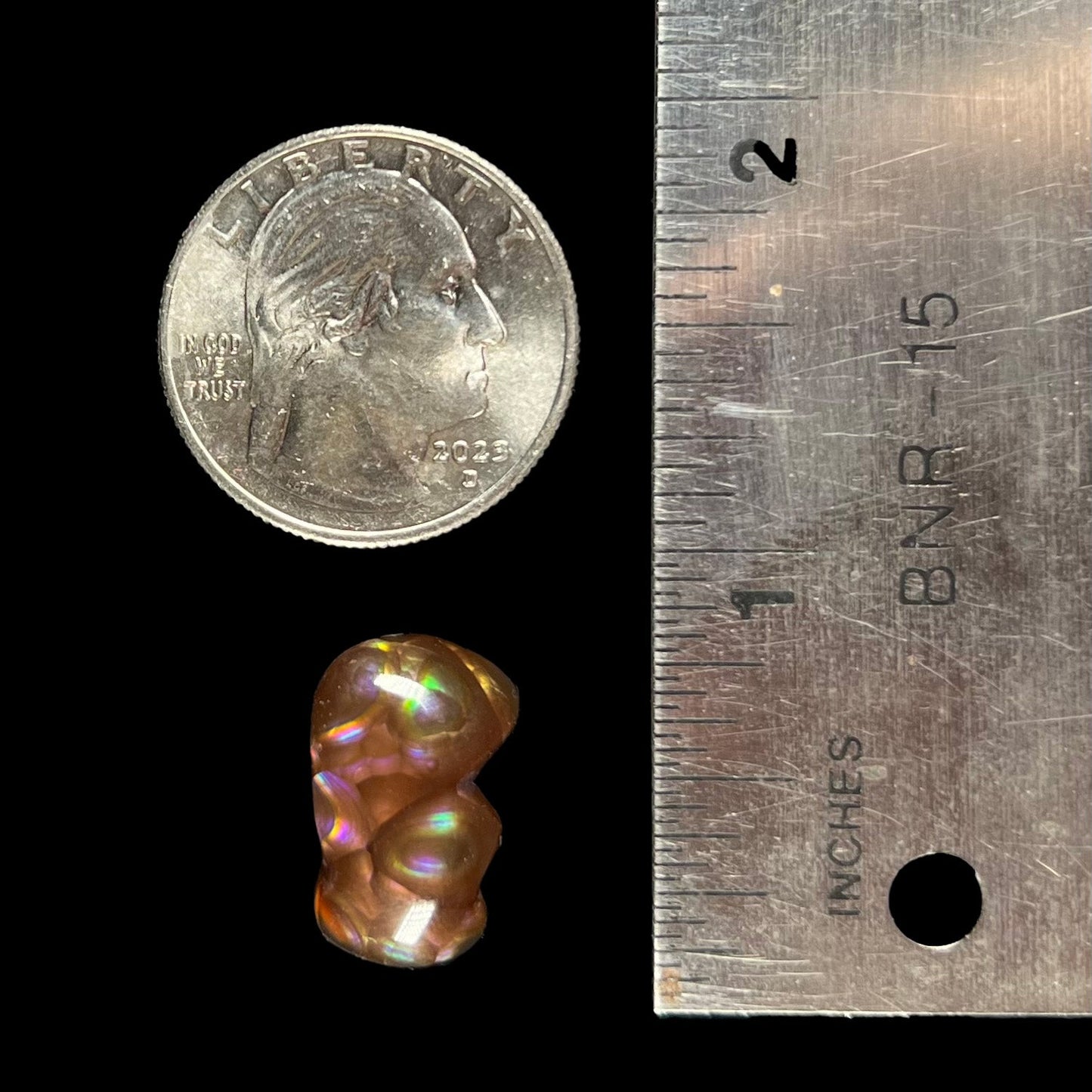A polished, freeform shaped fire agate stone. The stone is purple, green, and blue with red and yellow banding.