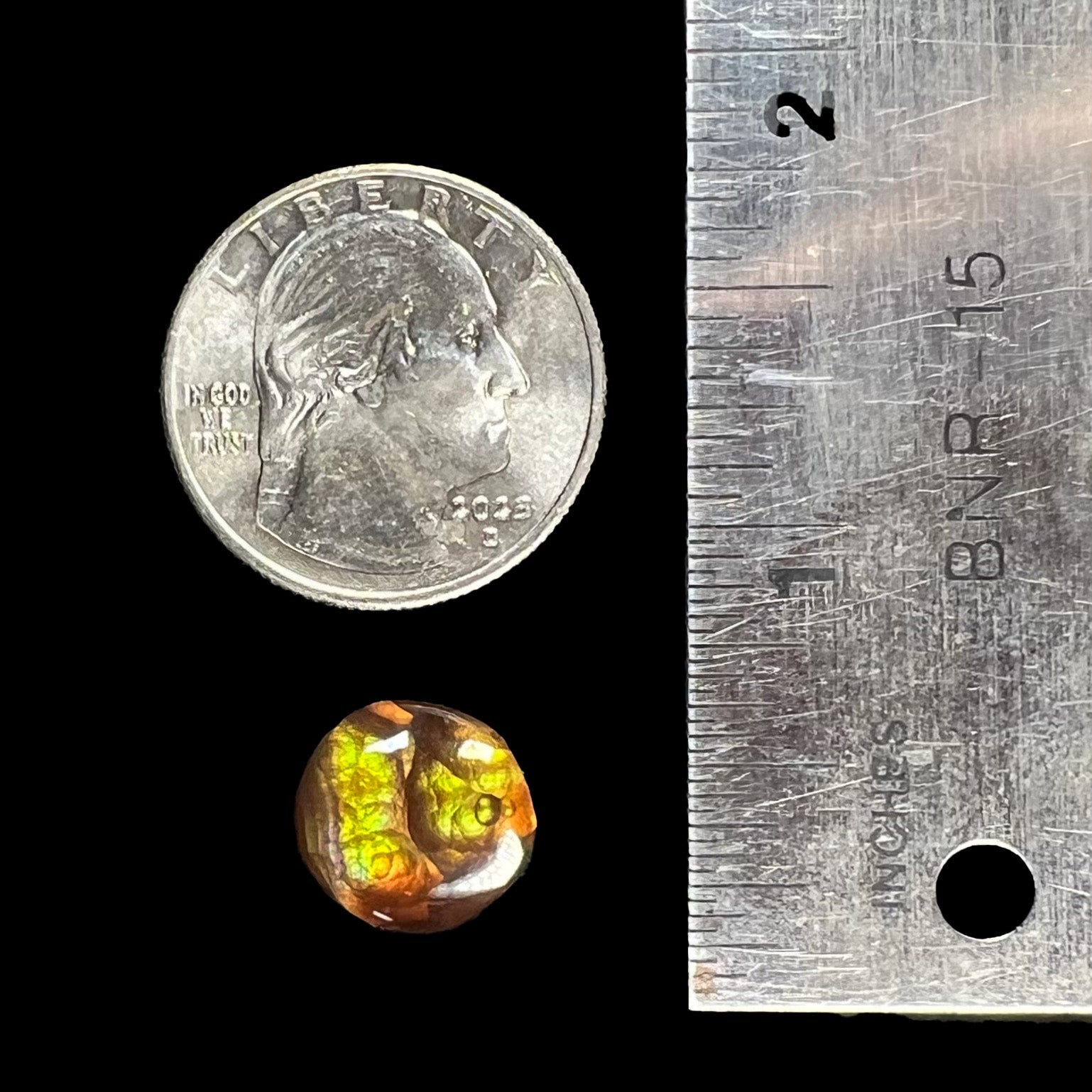 A loose, round cabochon cut fire agate stone.  The gem is green with orange, red, blue, and a purple stripe.