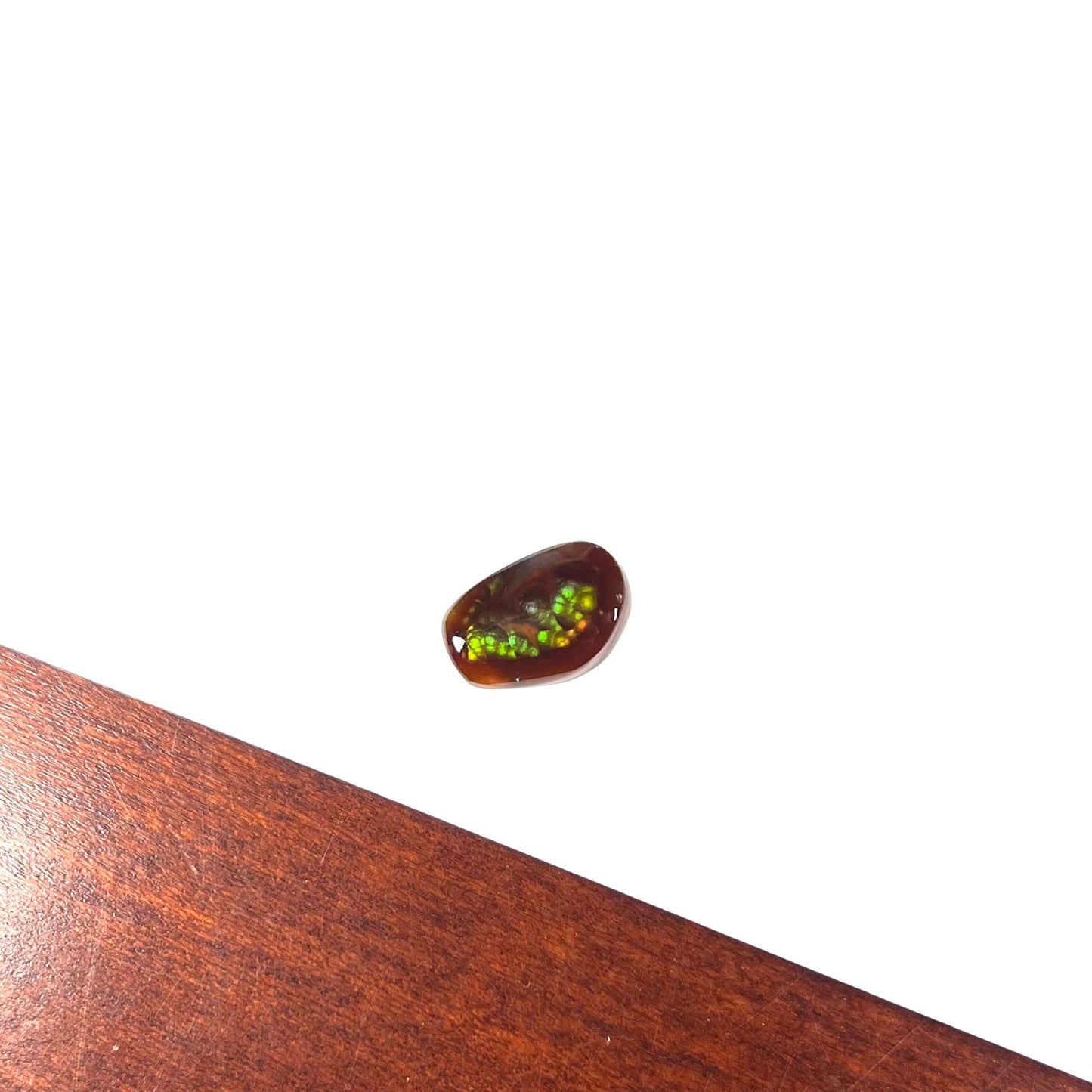 A loose, freeform cabochon cut fire agate gemstone. The stone is green with blue overtones.