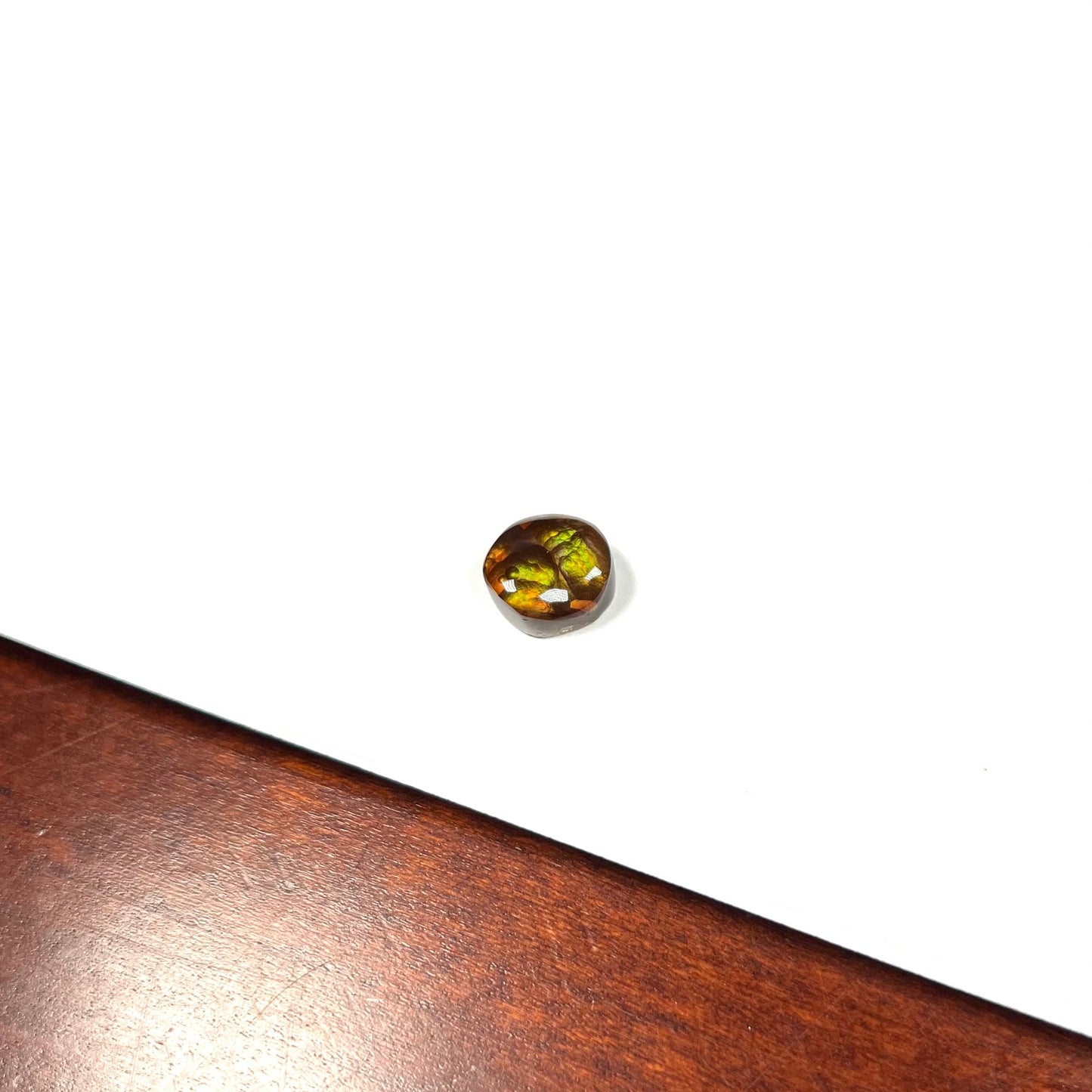 A loose, round cabochon cut fire agate stone. The gem is green with orange, red, blue, and a purple stripe.