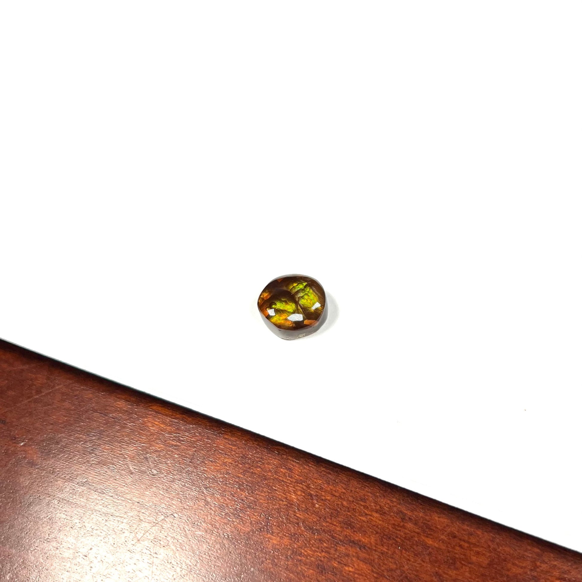 A loose, round cabochon cut fire agate stone.  The gem is green with orange, red, blue, and a purple stripe.