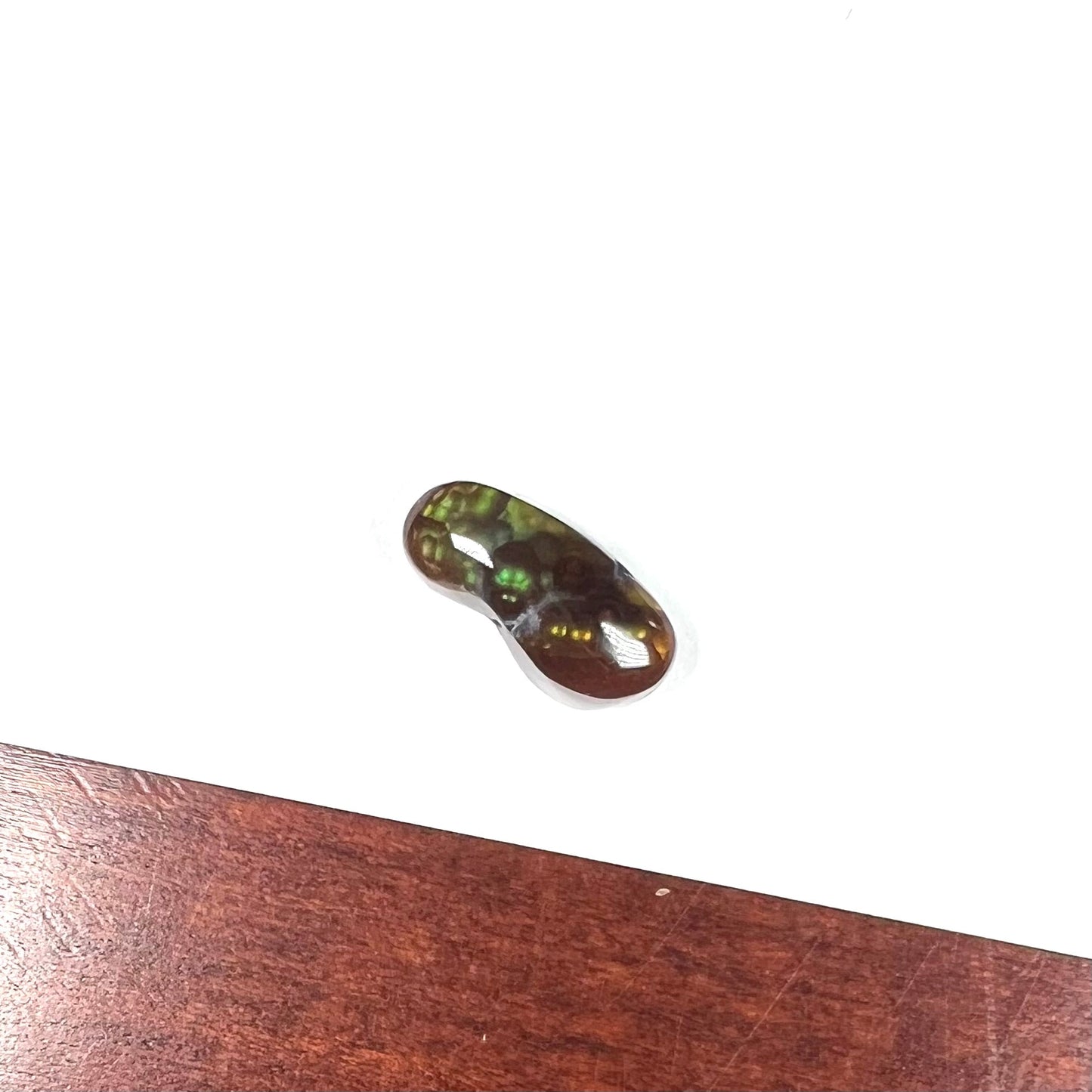 A loose, cabochon cut fire agate gemstone. The stone resembles a foot with a green heel and yellow toes.