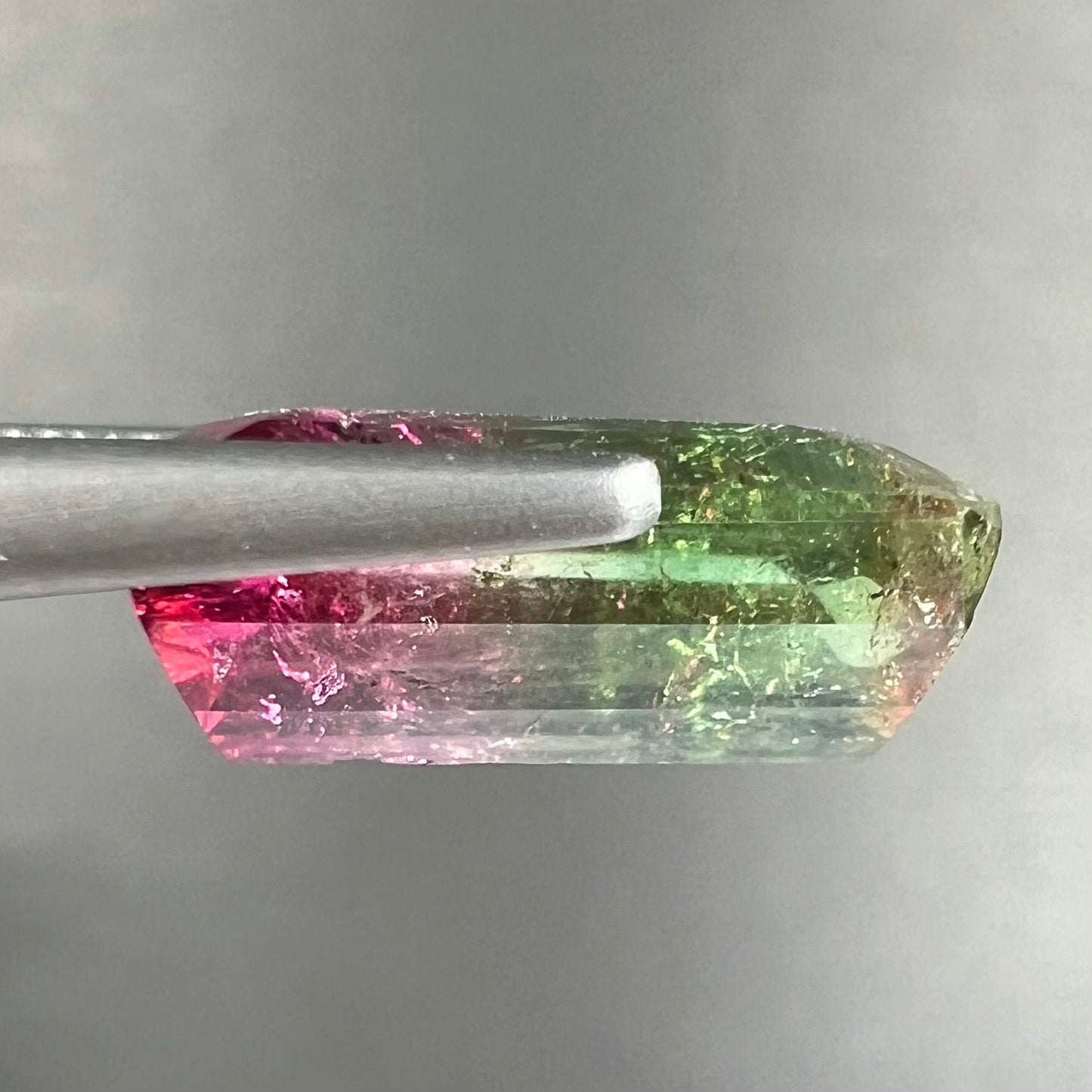 A loose watermelon tourmaline gemstone. The stone is emerald cut and fades from hot pink to green.