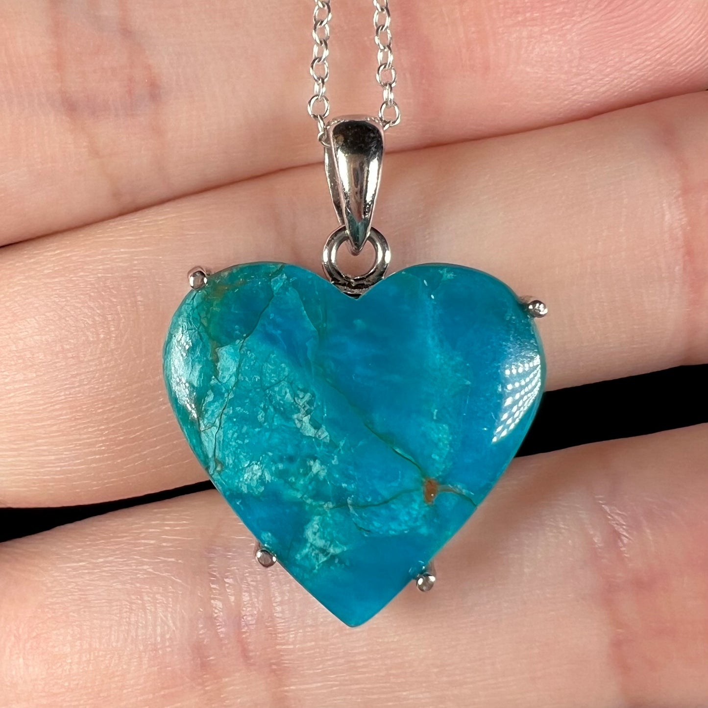 Macro view of natural blue opal heart necklace resting on fingers.