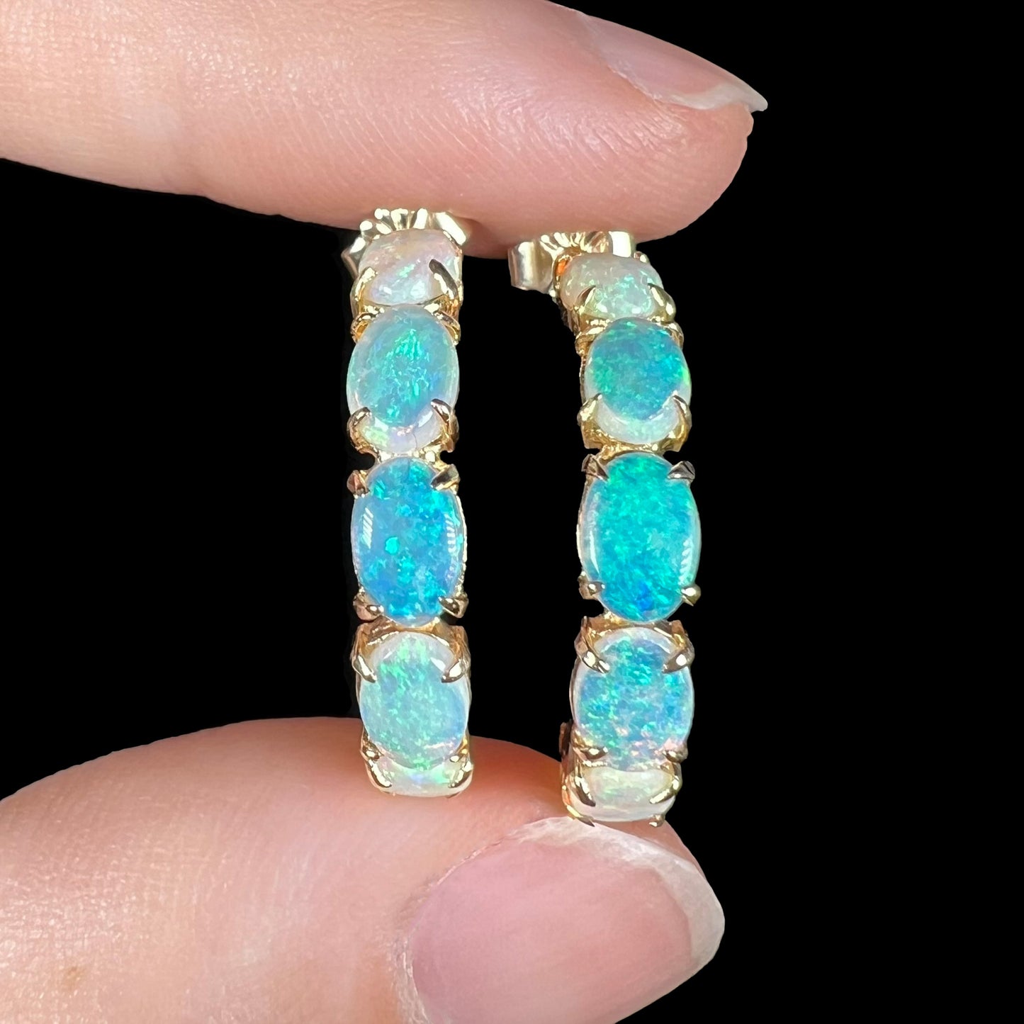 Close-up of gold opal earrings on fingers showing subtle blue and green flashes.