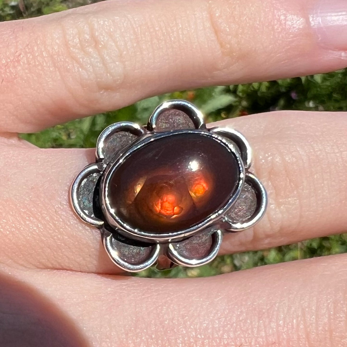 Macro view of fire agate ring in sun, reddish-orange flash visible.
