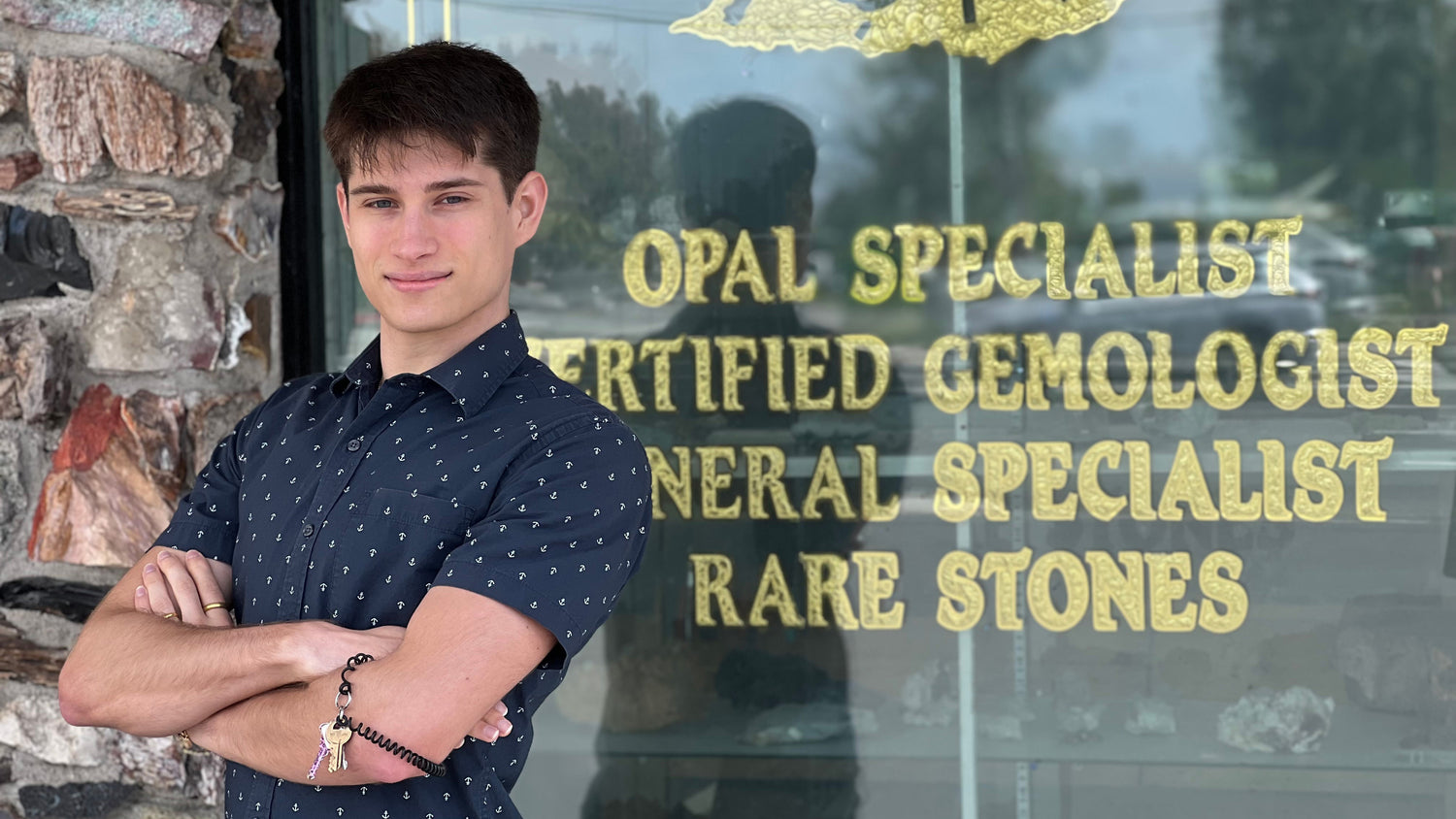 Certified Gemologist, Matthew Lervold, standing with arms crossed in front of a window with the text "Opal Specialist" showing.
