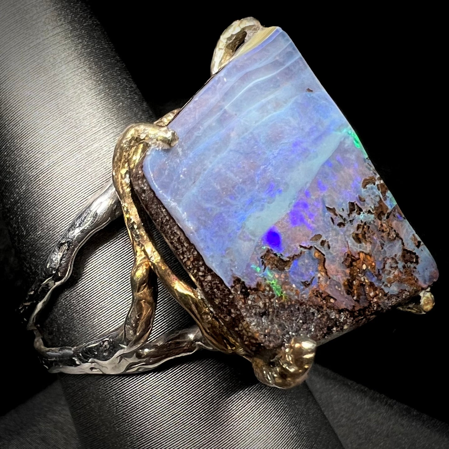 A maximalist-style boulder opal ring with an organic design, shown at an angle against a black background.