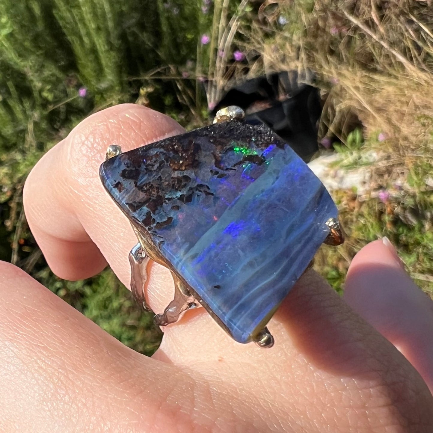 A maximalist-style silver boulder opal ring shown at an angle, worn on a hand in natural daylight.