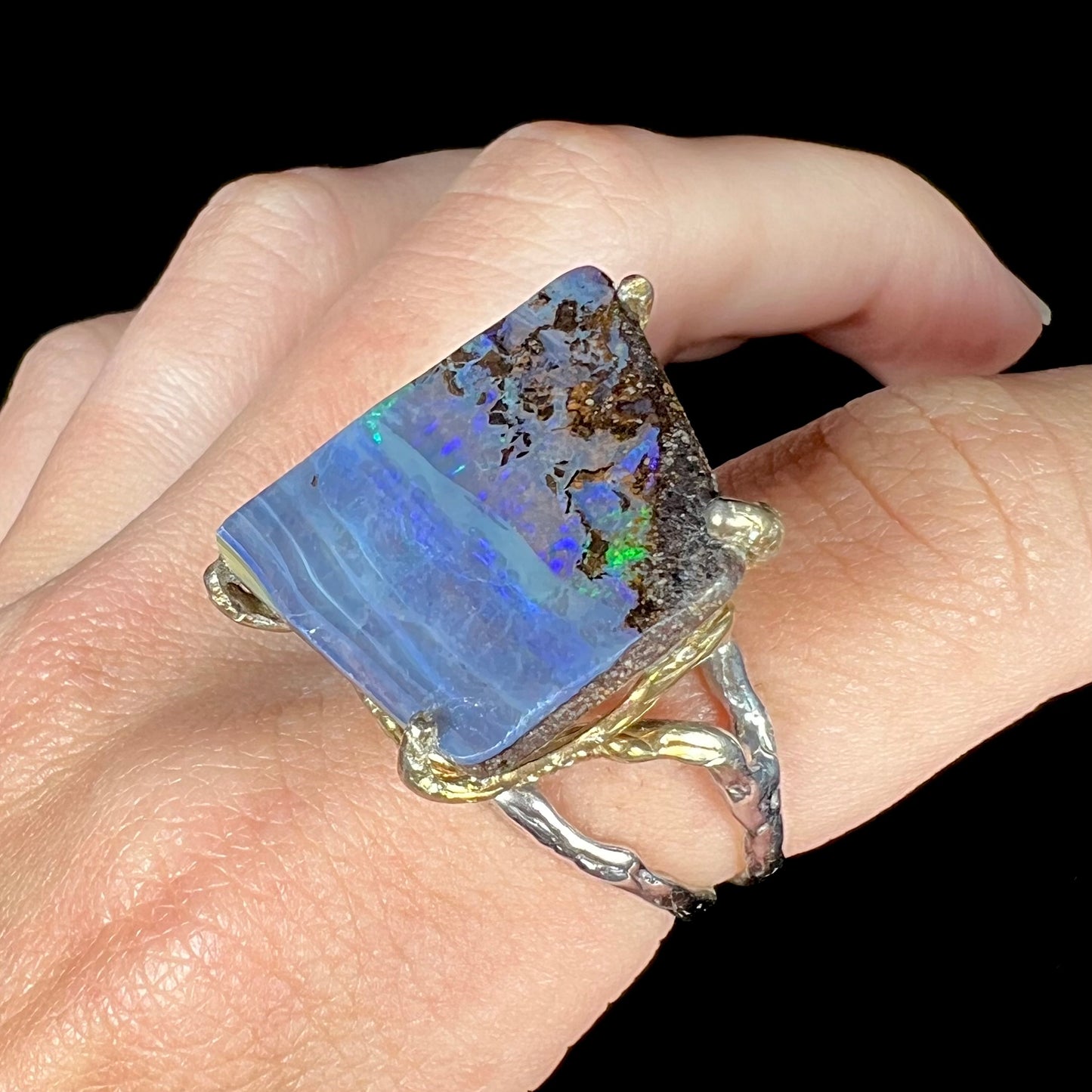 A maximalist-style ring set with an Australian boulder opal, worn on a finger and shown at an angle.