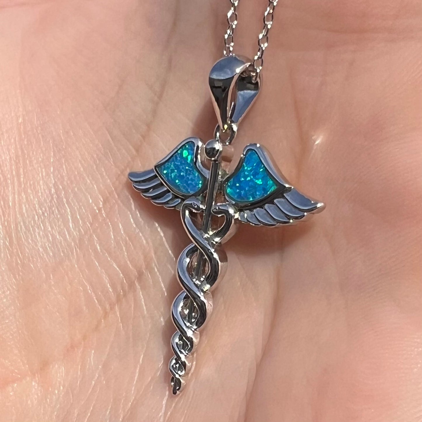 A silver plated medical caduceus pendant with blue lab-created opal inlay.